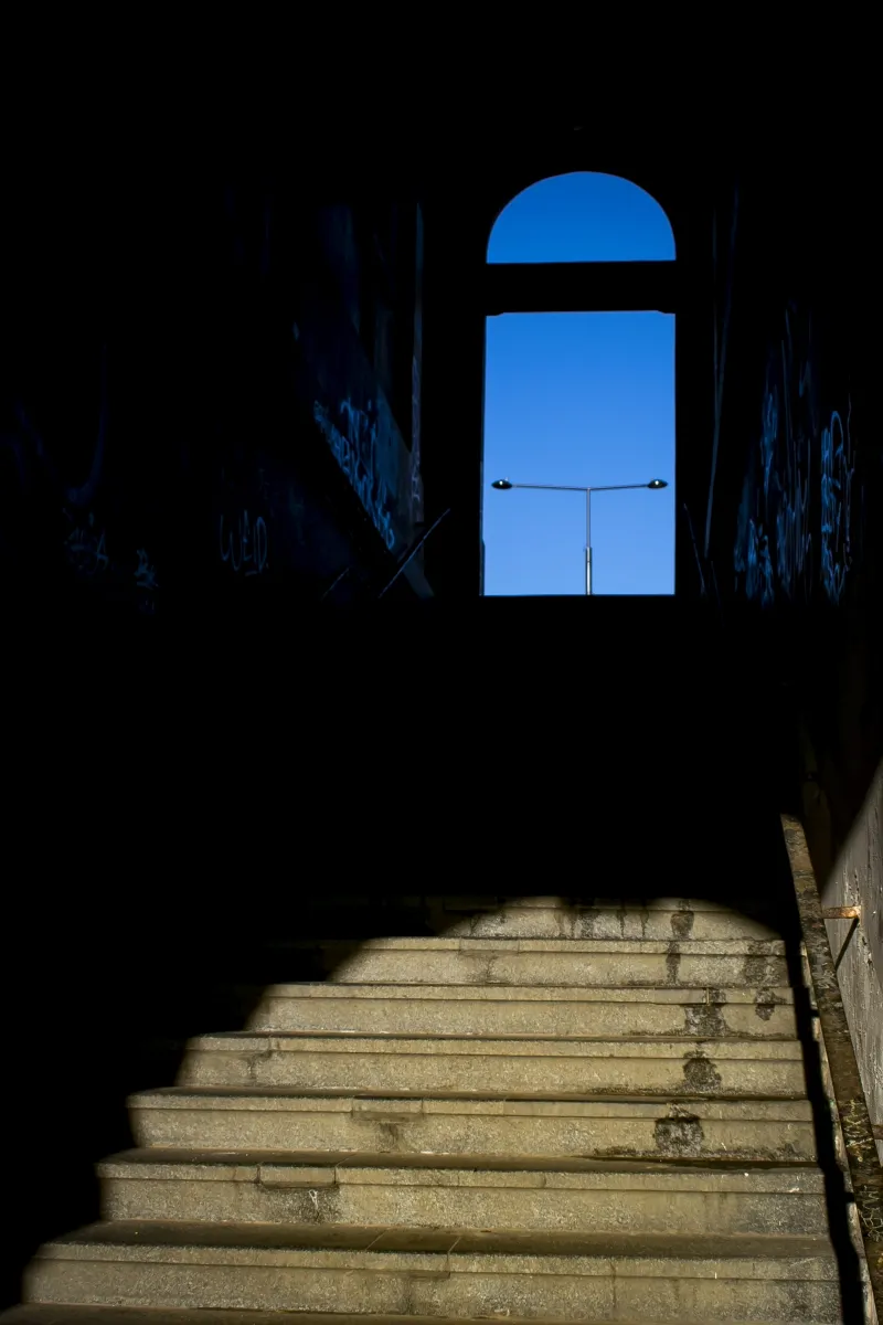 Dark stairway leading up to a bright blue window
